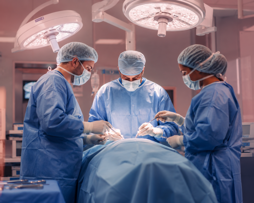 Three surgeons in blue scrubs and masks perform an operation under bright overhead lights.